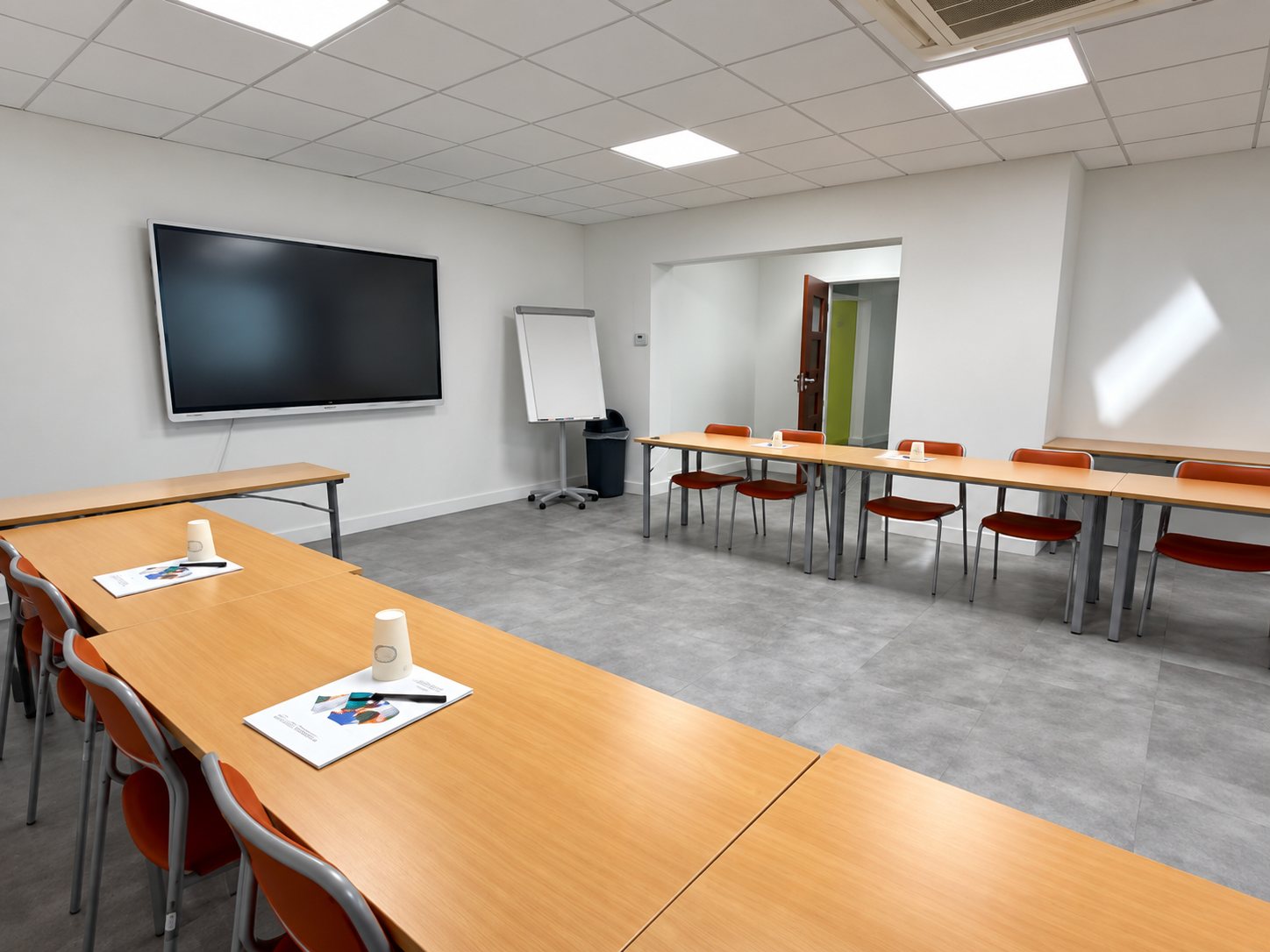 Salle de formation avec tables en bois, écran et paperboard